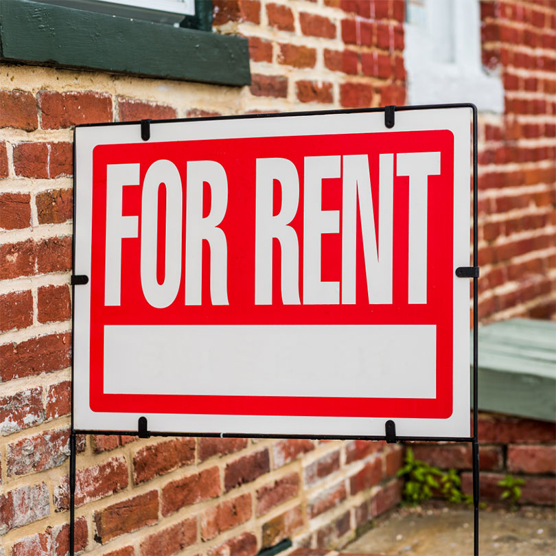 A red and white “for rent” sign with a brick background.